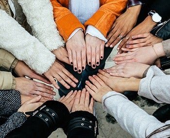 Hands of all different races placed in the middle of a circle.