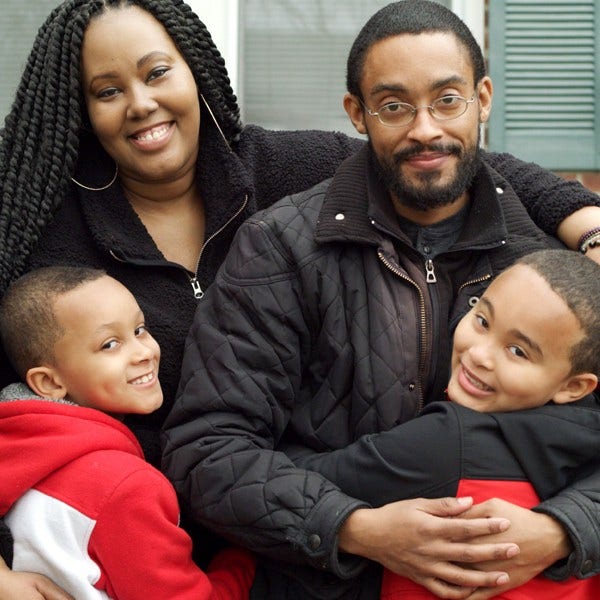 black male wearing glasses hugging wife and kids