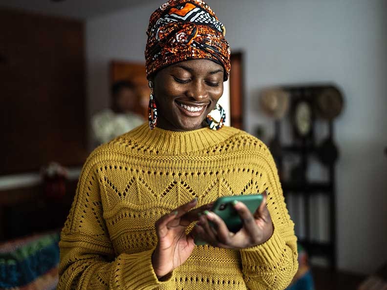 Woman smiling looking at her phone wearing a headscarf and yellow sweater