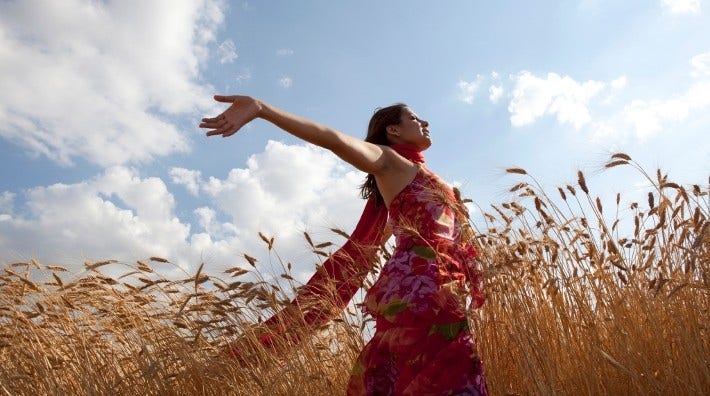 happy woman walks through a field of wheat with arms outstretched