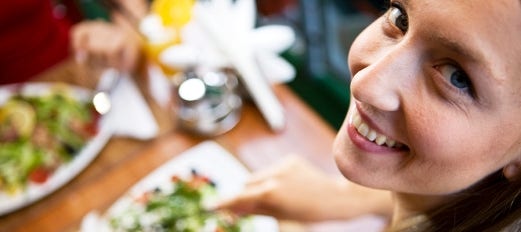 smiling woman sits at table and eats salad