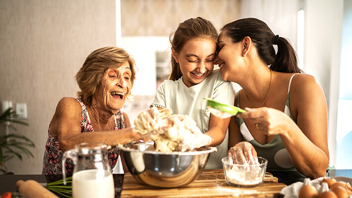 3 women laughing, smiling while preparing food in a kitchen